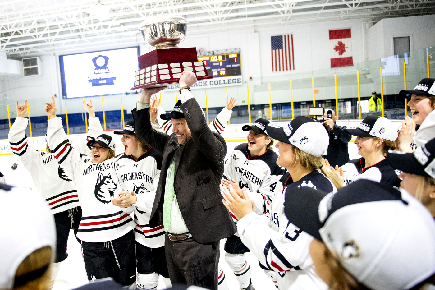 Northeastern coach Dave Flint raises a trophy surrounded by his players.