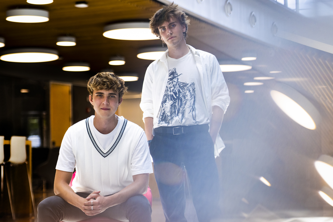 two students wearing white shirts, one sitting on the left and one standing on the right