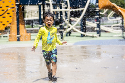 Boston resident, Aramis Acevedo, (not pictured) watches his son play at the William E. Carter Playground water feature. Photo by Matthew Modoono/Northeastern University