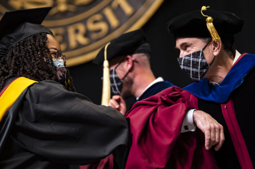 David Madigan (right), Northeastern's provost and senior vice president, elbow-bumps a College of Professional Studies master's graduate as she receives her degree during the ceremony at Matthews Arena.  Photo by Alyssa Stone/Northeastern University