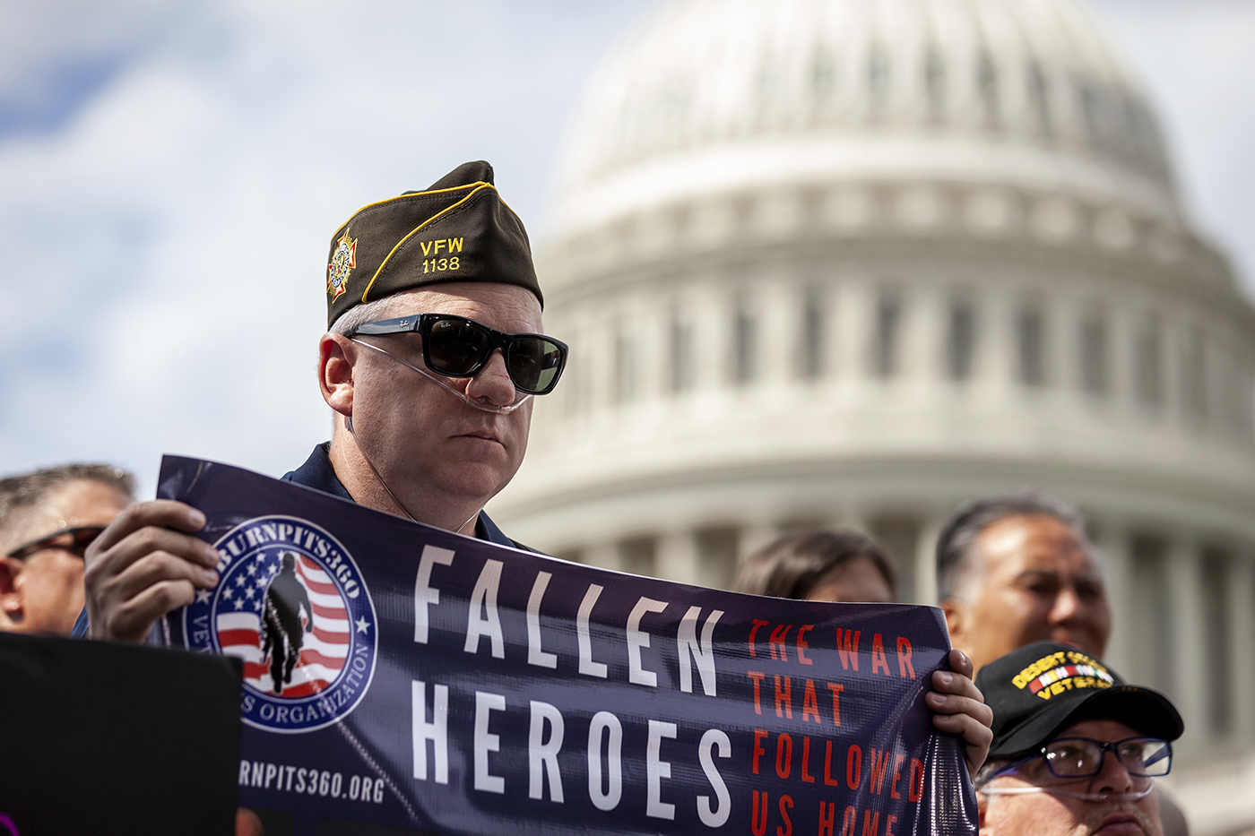 man holding a blue banner that says fallen heroes in all caps on it