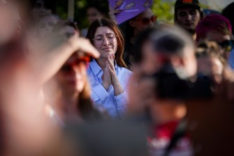 woman in blue shirt stands in a crowd with her hands together in prayer