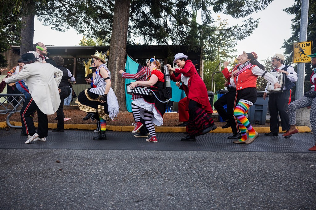 line of actors in various costumes dances on a sidewalk