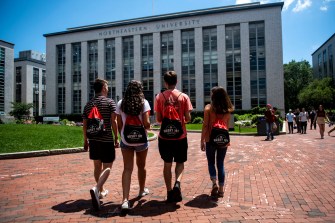 four students stand arm in arm in front of university building