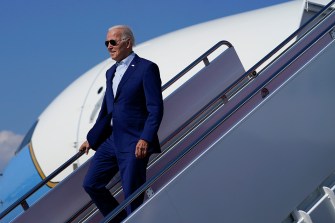president biden walking down the steps of a plain wearing blue suit and aviator sunglasses