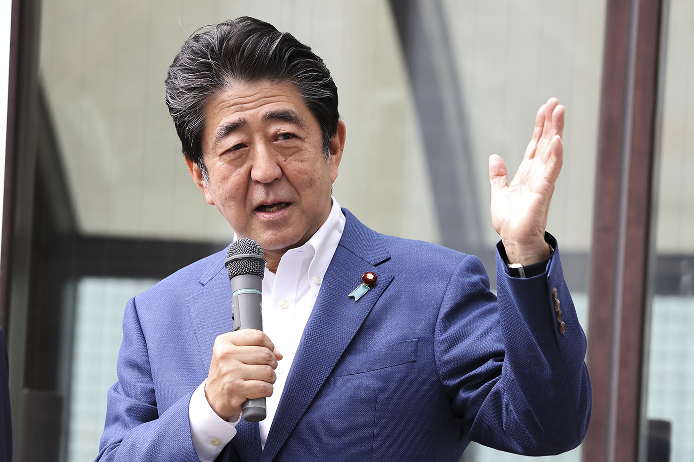 japanese man in blue suit speaking into microphone and gesturing with his hand