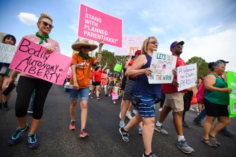 protestors carrying pink and white signs walk down a street