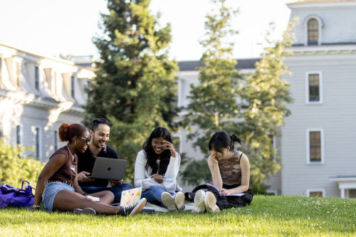 group of people sits on college campus lawn