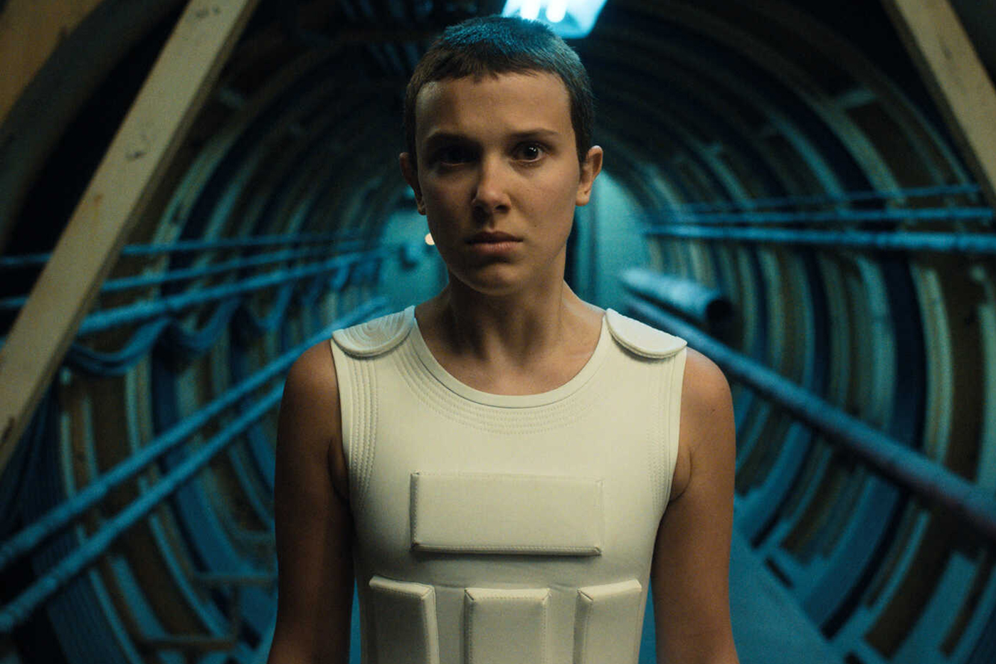 Eleven from Stranger Things in a military-style vest and inside a tunnel or bunker