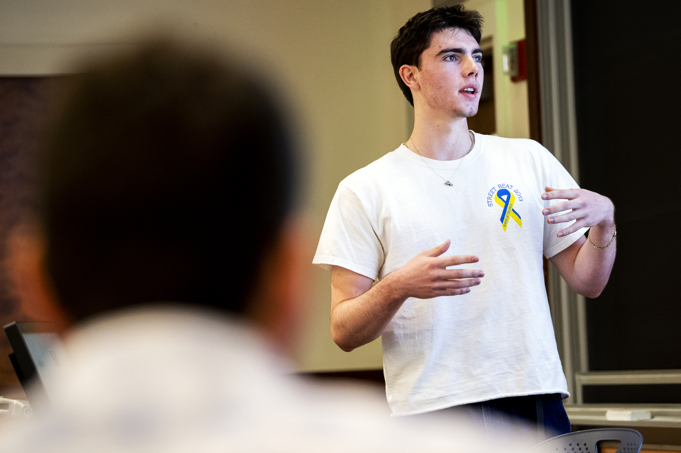 student wearing white t-shirt gesturing with his hands while presenting
