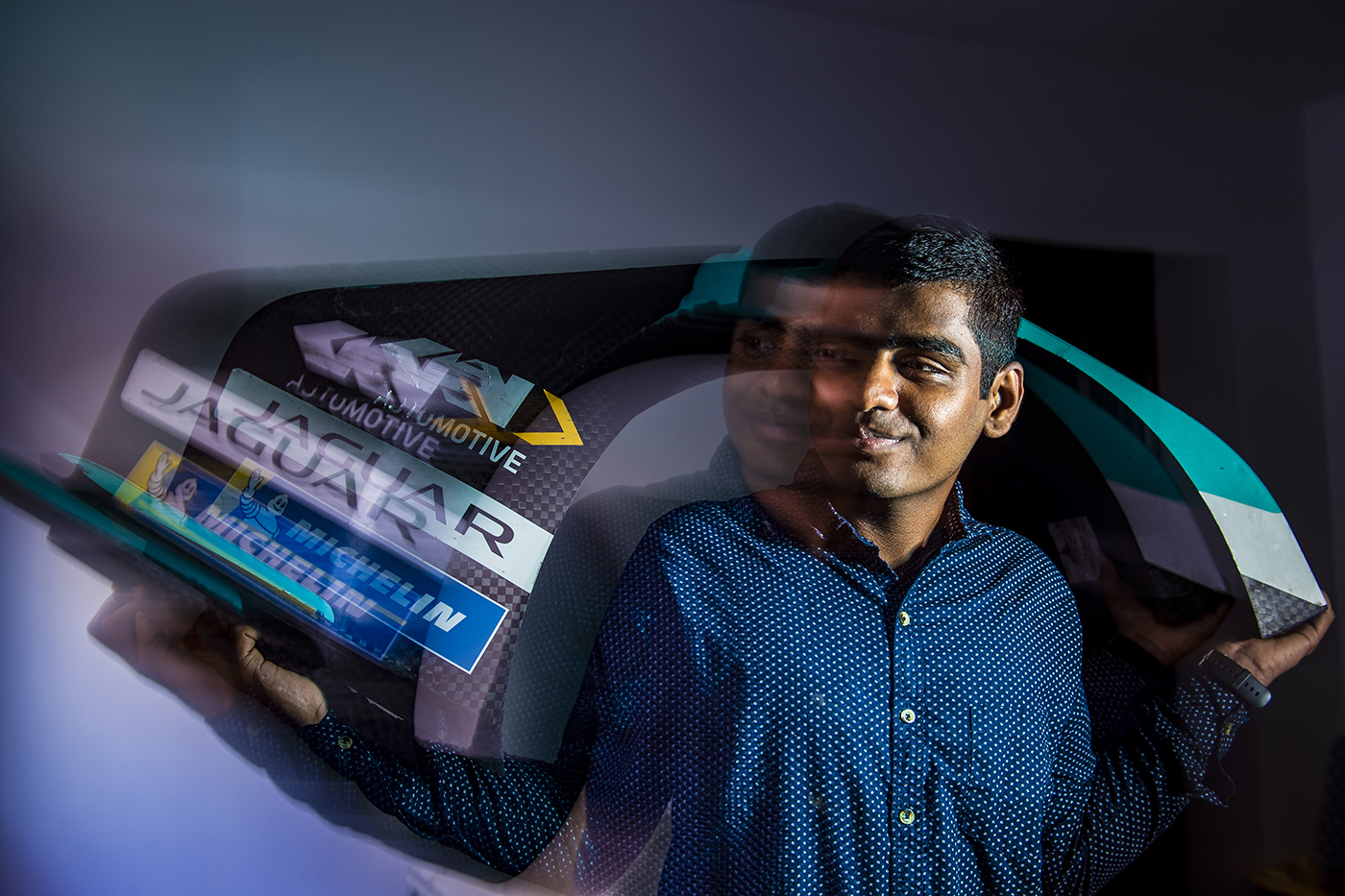 Omkar Ligade, a master's student in engineering, poses for a portrait at his Roxbury apartment with the fender of a Formula E race car.