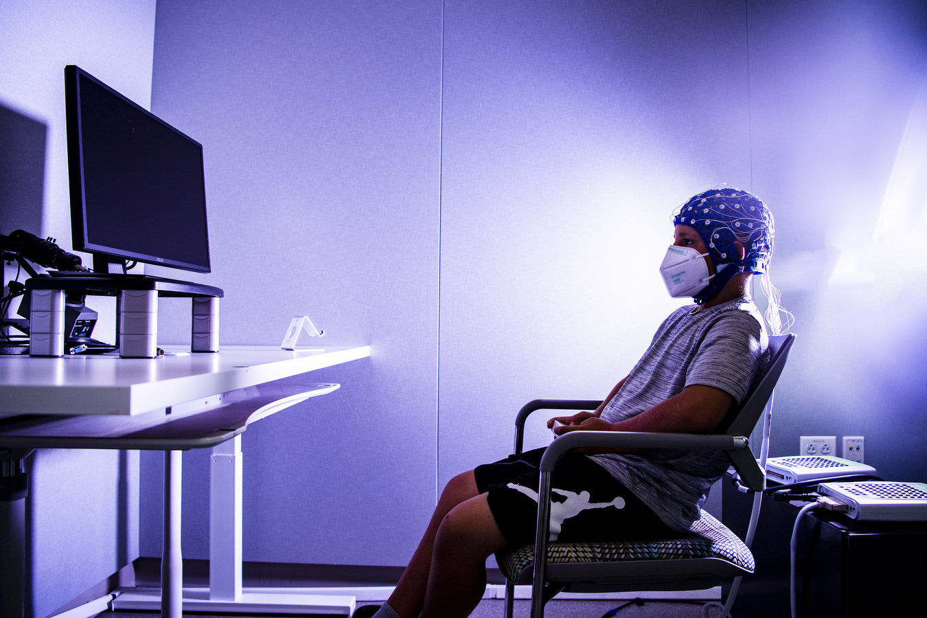 A study participant wearing a cap with sensors looks at a TV screen