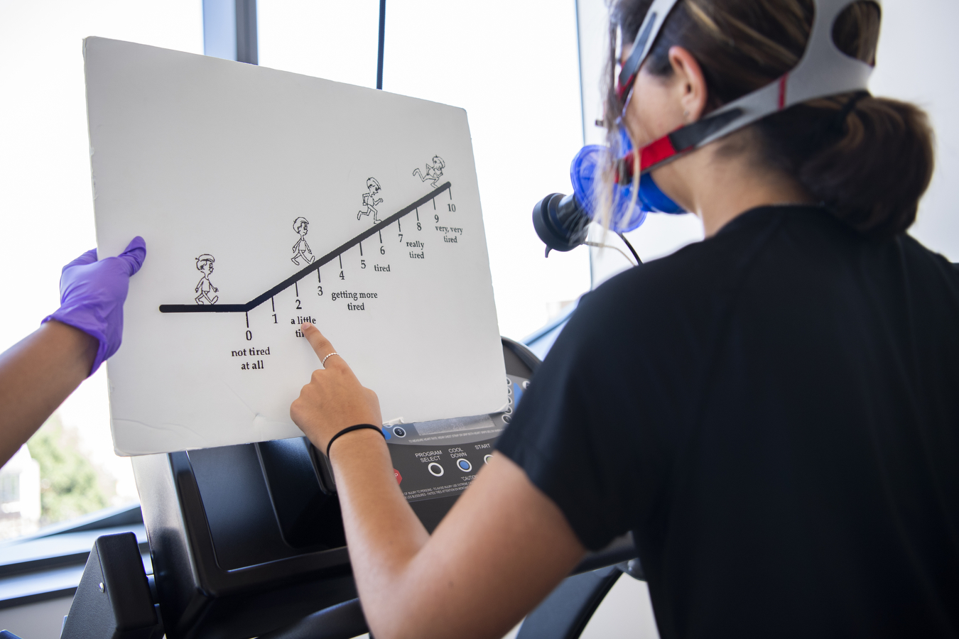 A study participant wearing a device that measures aerobic capacity around the face points to a number on a chart held out in front of them