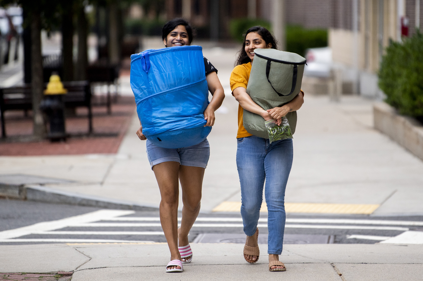 Two students have smiles on their faces as they carry clothing hampers down the sidewalk