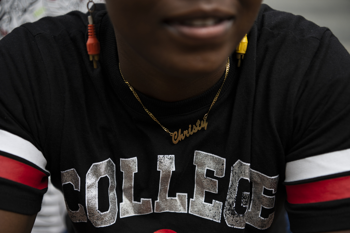 A closeup of the lower half of a person's face who's wearing a black shirt and red and orange earrings.