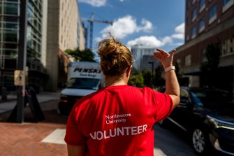 A person wearing a shirt that says 'Volunteer' in large letters on the back directs a car in traffic by waving a hand