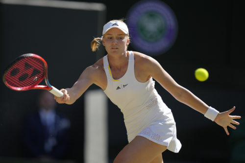 woman wearing all white tennis outfit swinging for a tennis ball