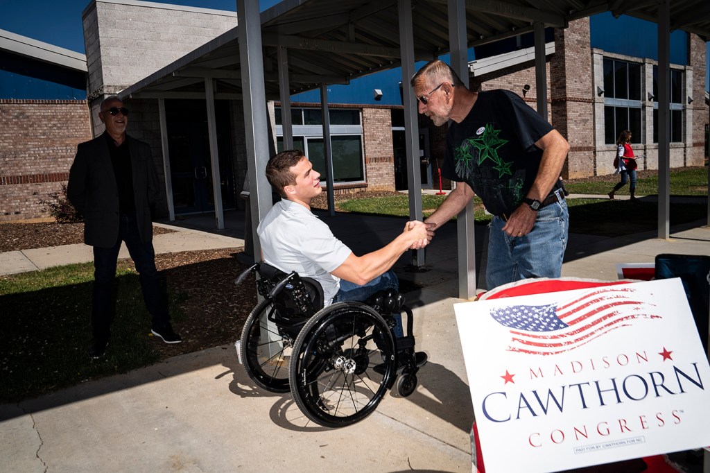 man standing up shaking the hand of a man in a wheelchair