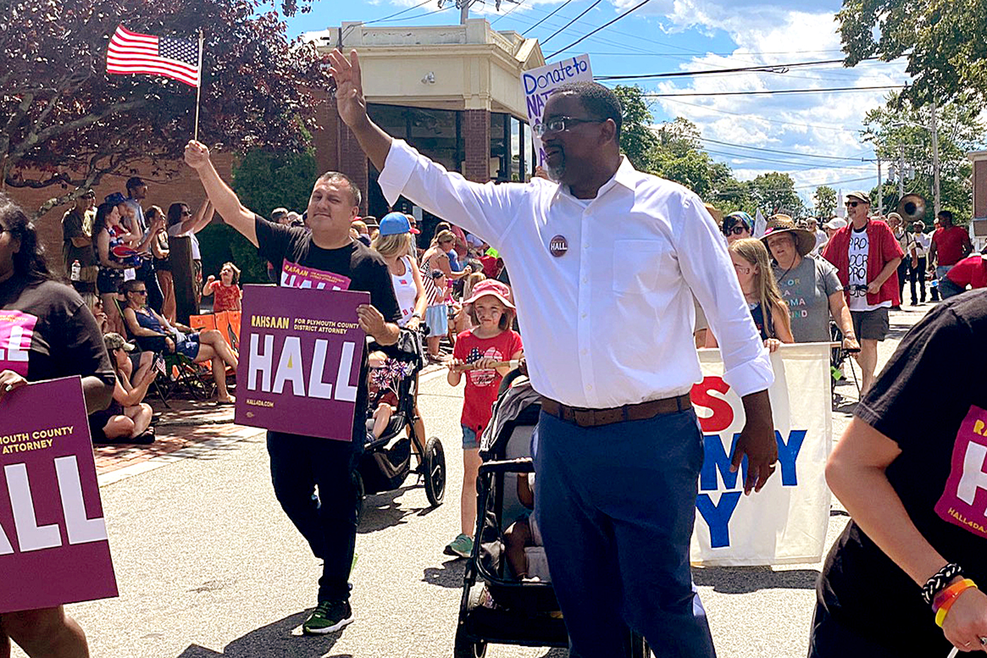 Rahsaan Hall waves to the crowd as he walks in a parade surrounded by supporters carrying signs bearing his name and carrying American flags
