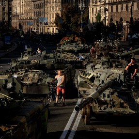 People walk among destroyed military vehicles on a city street