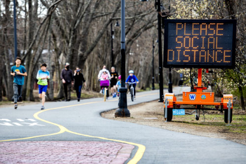 People are running outside near a large sign with orange text over a black background: 