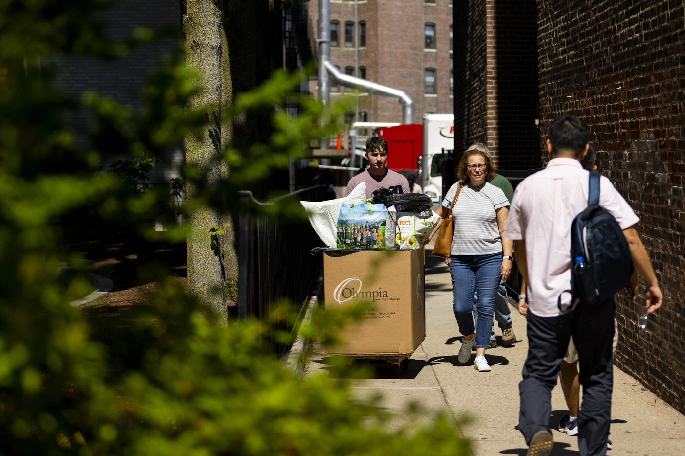 Parents of college students are walking outside with a bin filled with dorm supplies. 