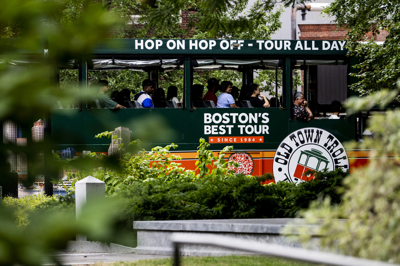 A bus riding through a city has white text over a green background: "Boston's Best Tour." 