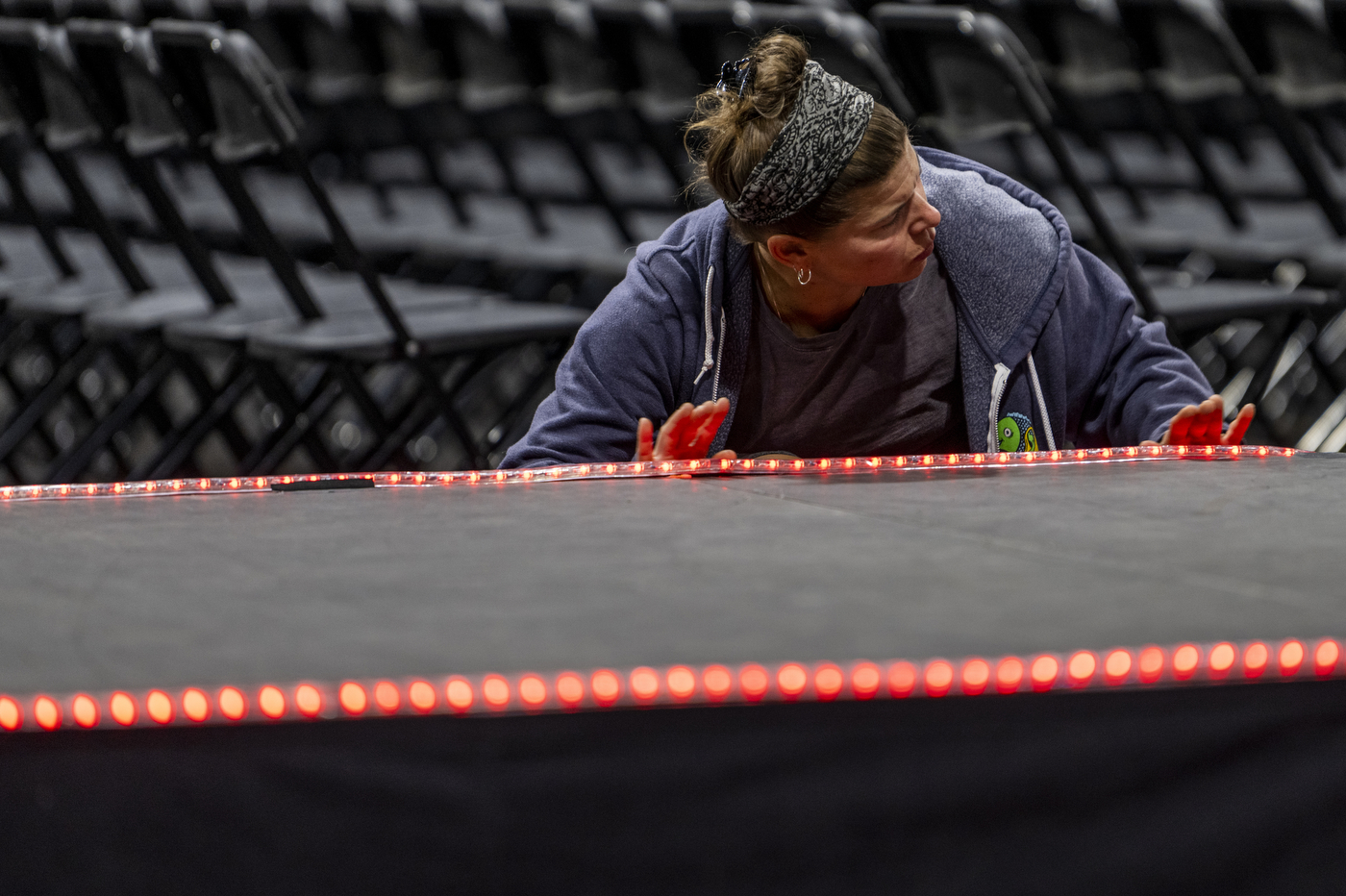 A person is wearing a blue hoodie and a grey shirt while leaning over a row of small red lights to get ready for Northeastern's Convocation.