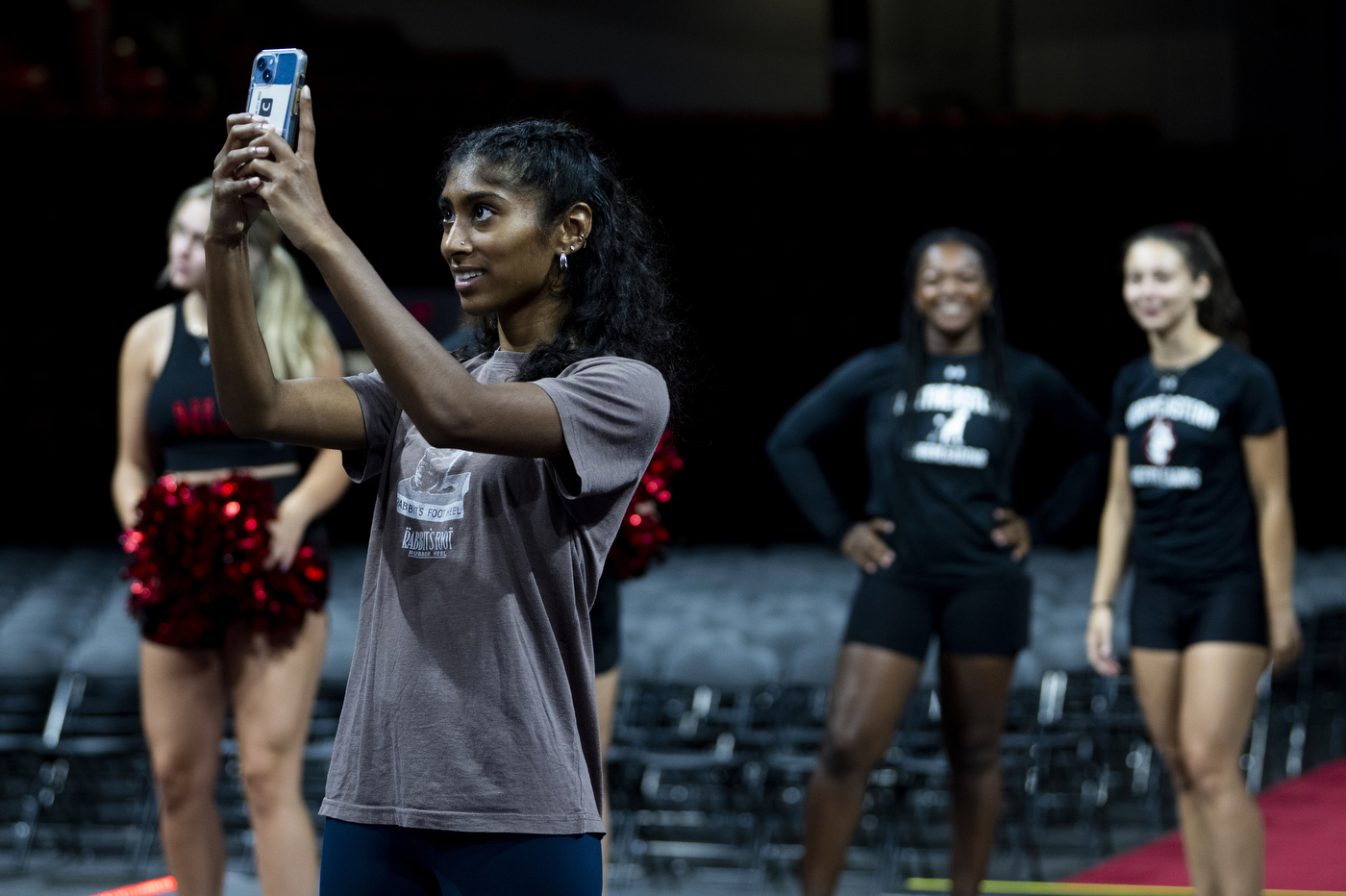 A person wearing a grey shirt holds a phone to take a picture of Northeastern's Convocation. 