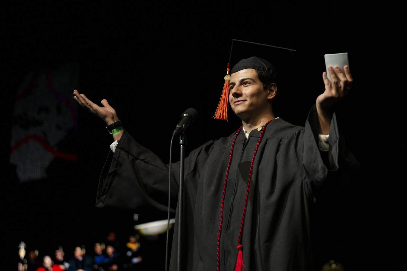 A person wearing a graduation cap and gown is talking into a microphone at Northeastern's 2022 Convocation.
