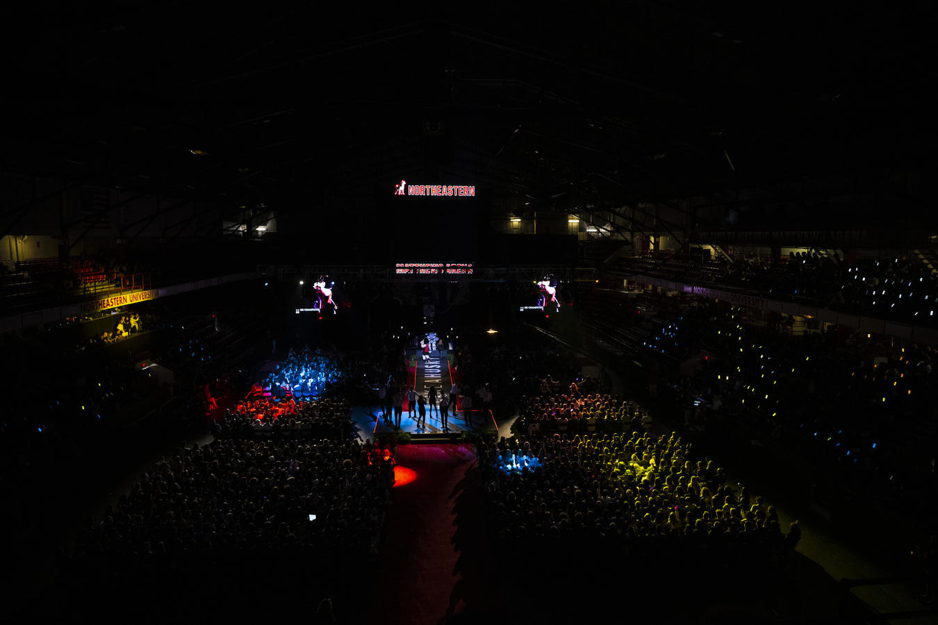 A large arena is dimly lit with colorful lights at Northeastern's 2022 Convocation. 