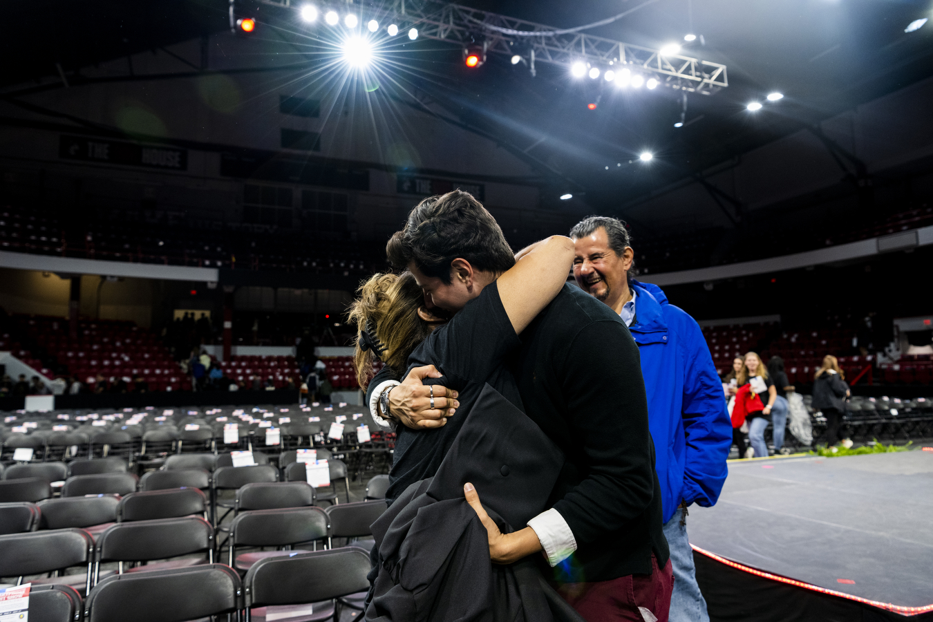 A family at Northeastern's Convocation are hugging while standing in a large arena. 