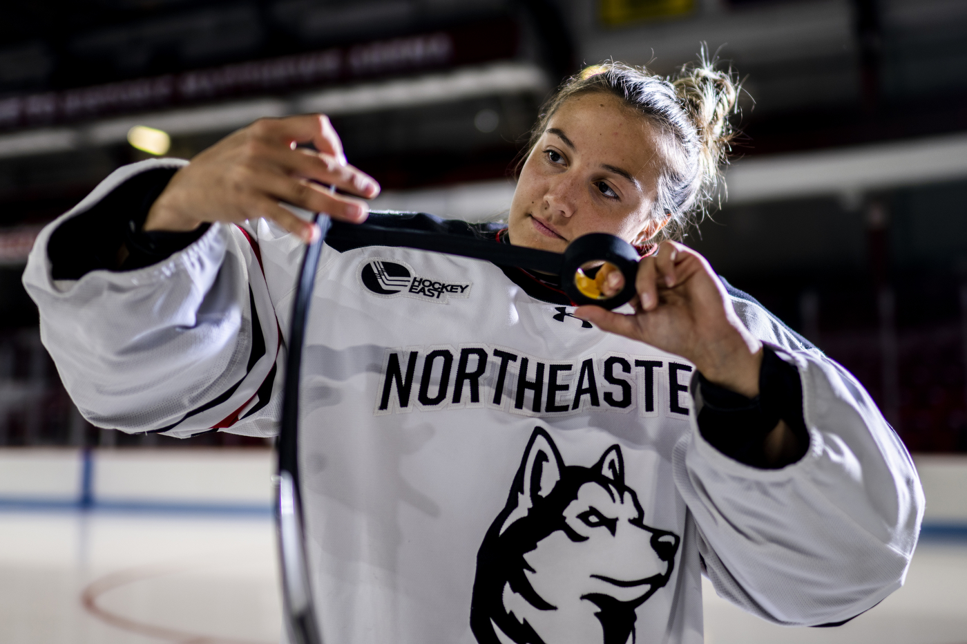 Gwyn Philips, wearing a Northeastern hockey jersey, wraps her hockey stick with black tape