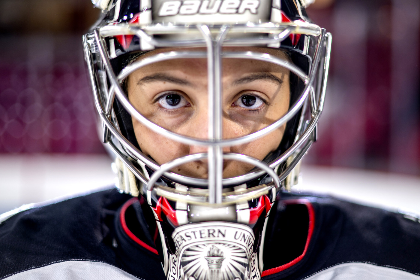 A closeup of Gwyn Philips, one the ice in her hockey gear and goalie mask, looking straight ahead