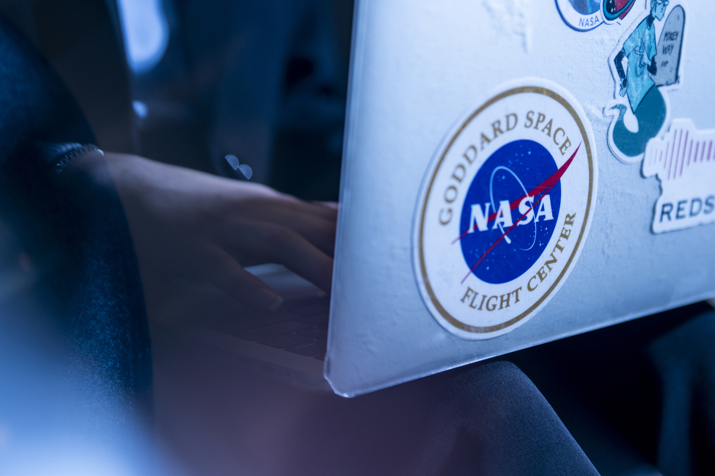 A person is working on a silver-colored laptop that has a large NASA sticker on the front. 