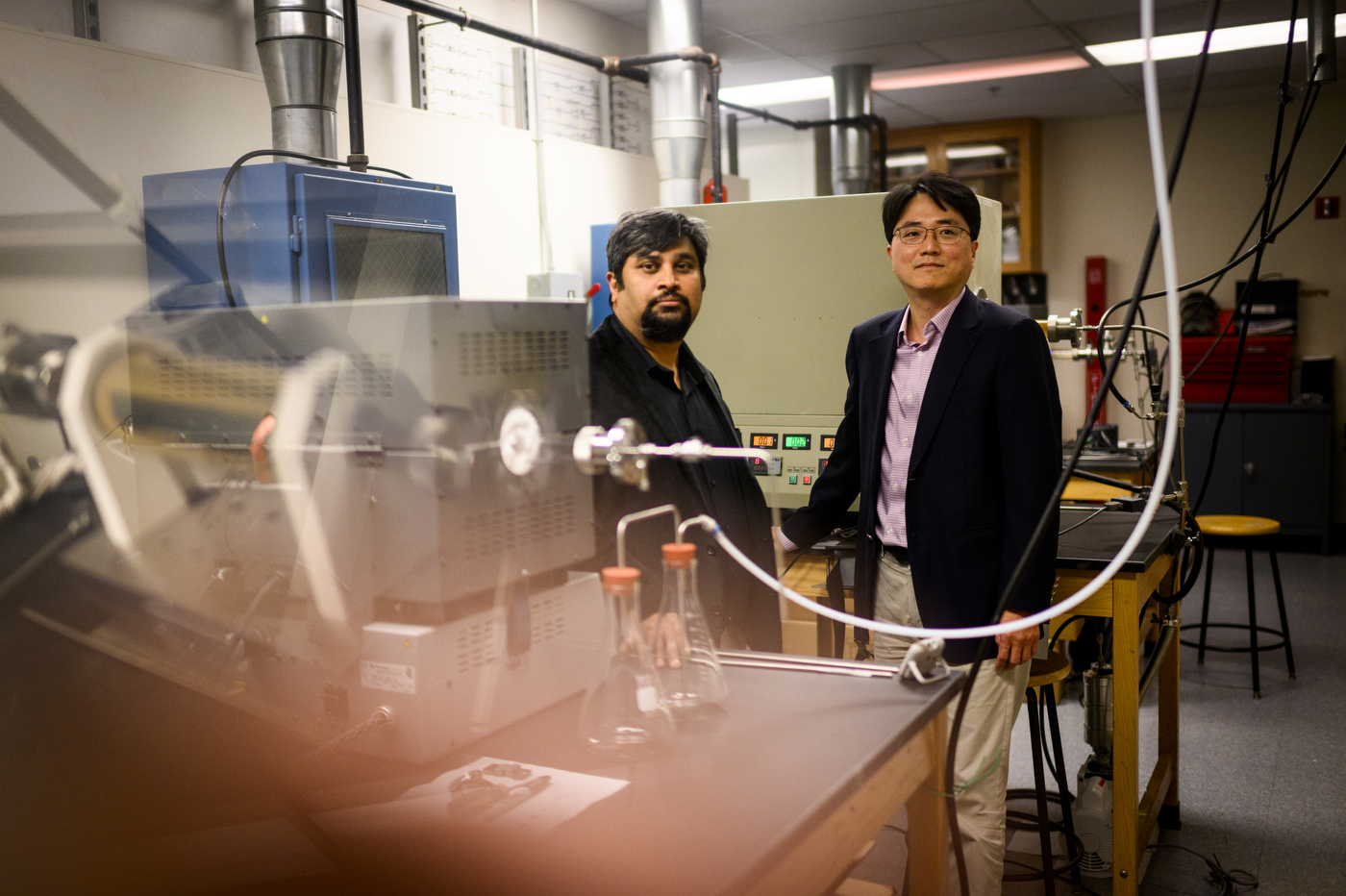 Two professors posing next to lab equipment