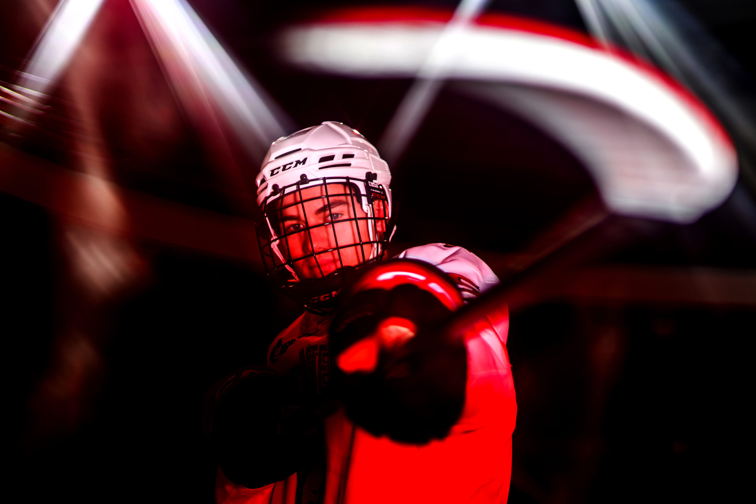 Hunter MacDonald holds a hockey stick out towards the camera wearing a hockey helment