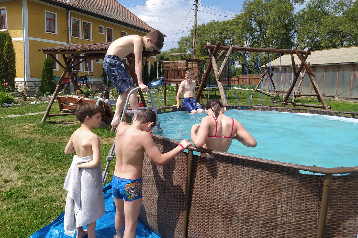 Children are swimming in an above-ground swimming pool outside on a sunny day. 