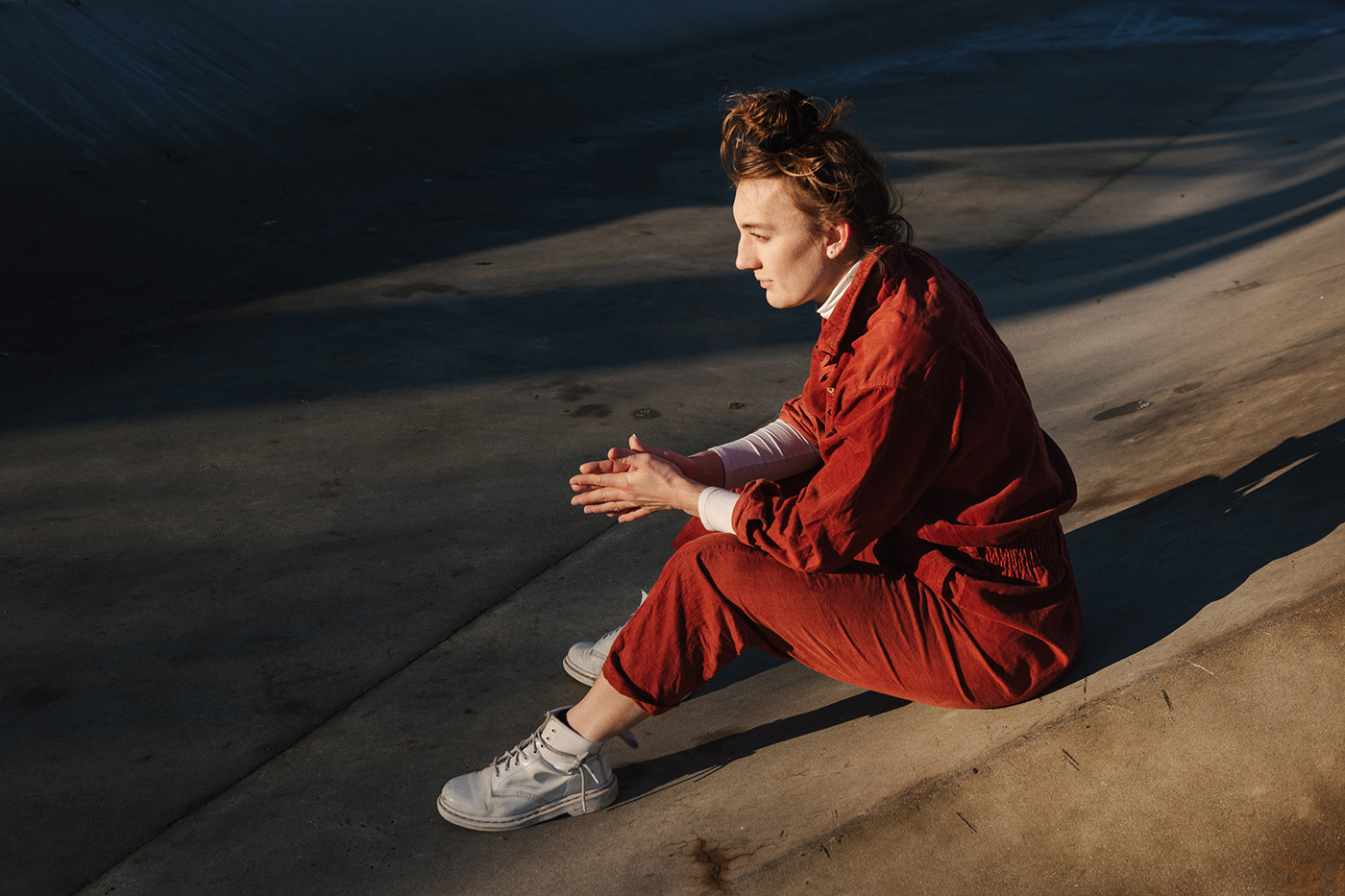A person wearing a red jumpsuit is sitting on the pavement in the sunlight.