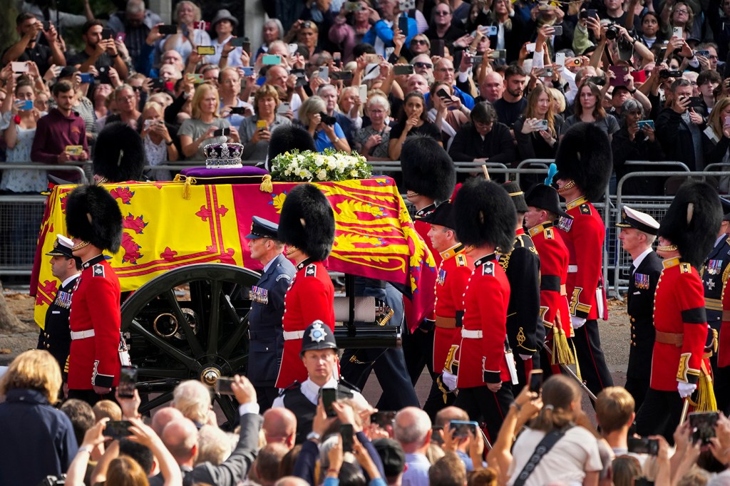 Queen Elizabeth II's coffin is escorted down a street lined with thousands or people.