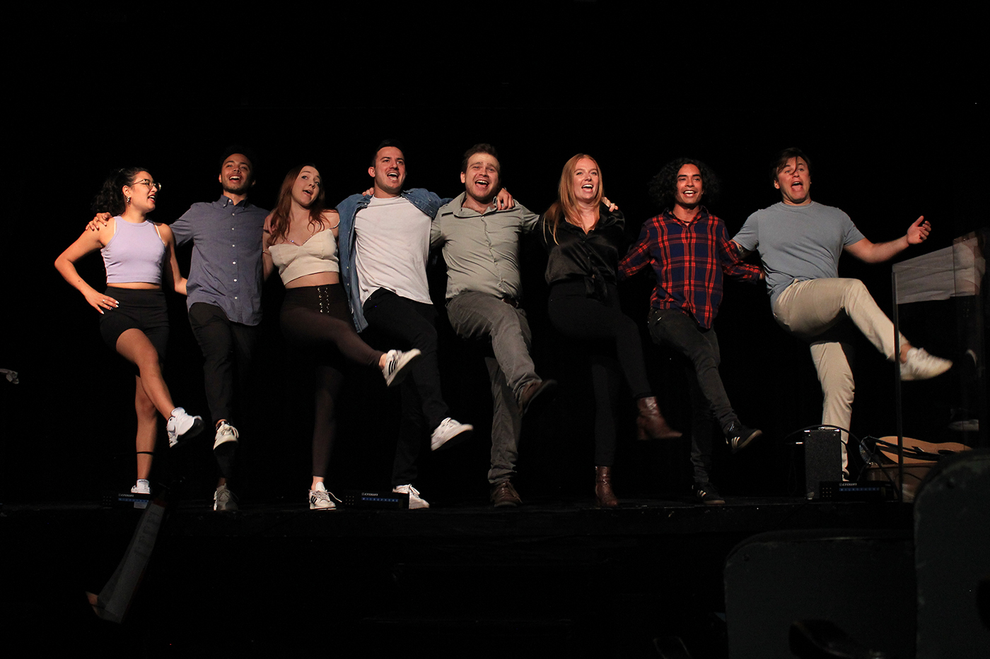 Multiple actors are dancing together on stage in the spotlight during a sketch comedy show. 