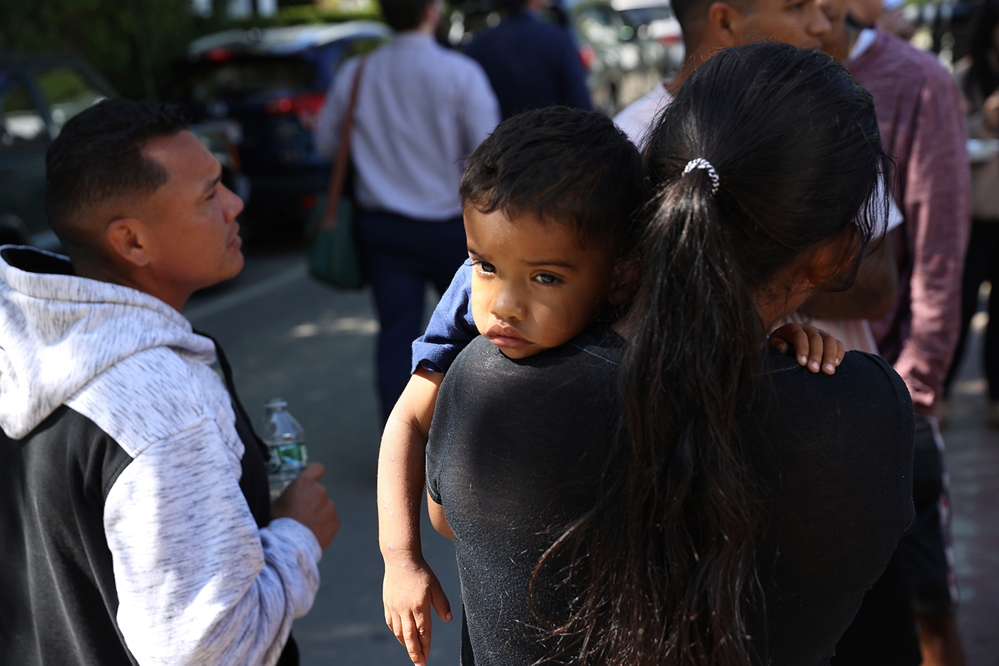 A person wearing a black jacket is holding a child while surrounded by people.ed by people.