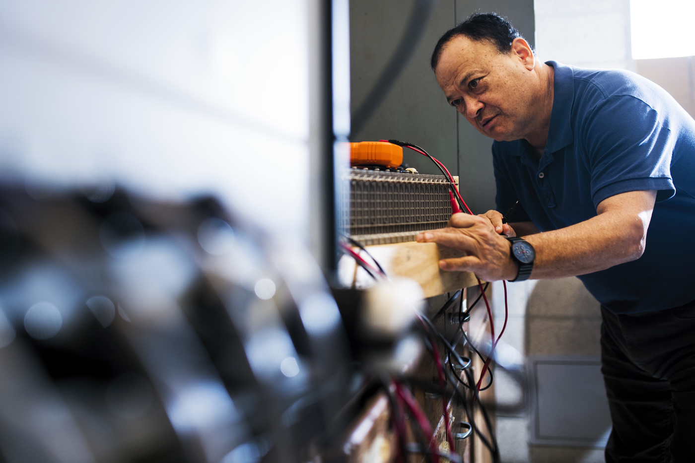 Eugene Smotkin evaluating a large, orange battery's performance after hooking it up to a larger machine