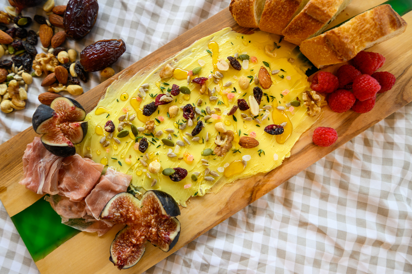 A butter board surrounded by bread, figs, dates, nuts, raspberries, and other snacks
