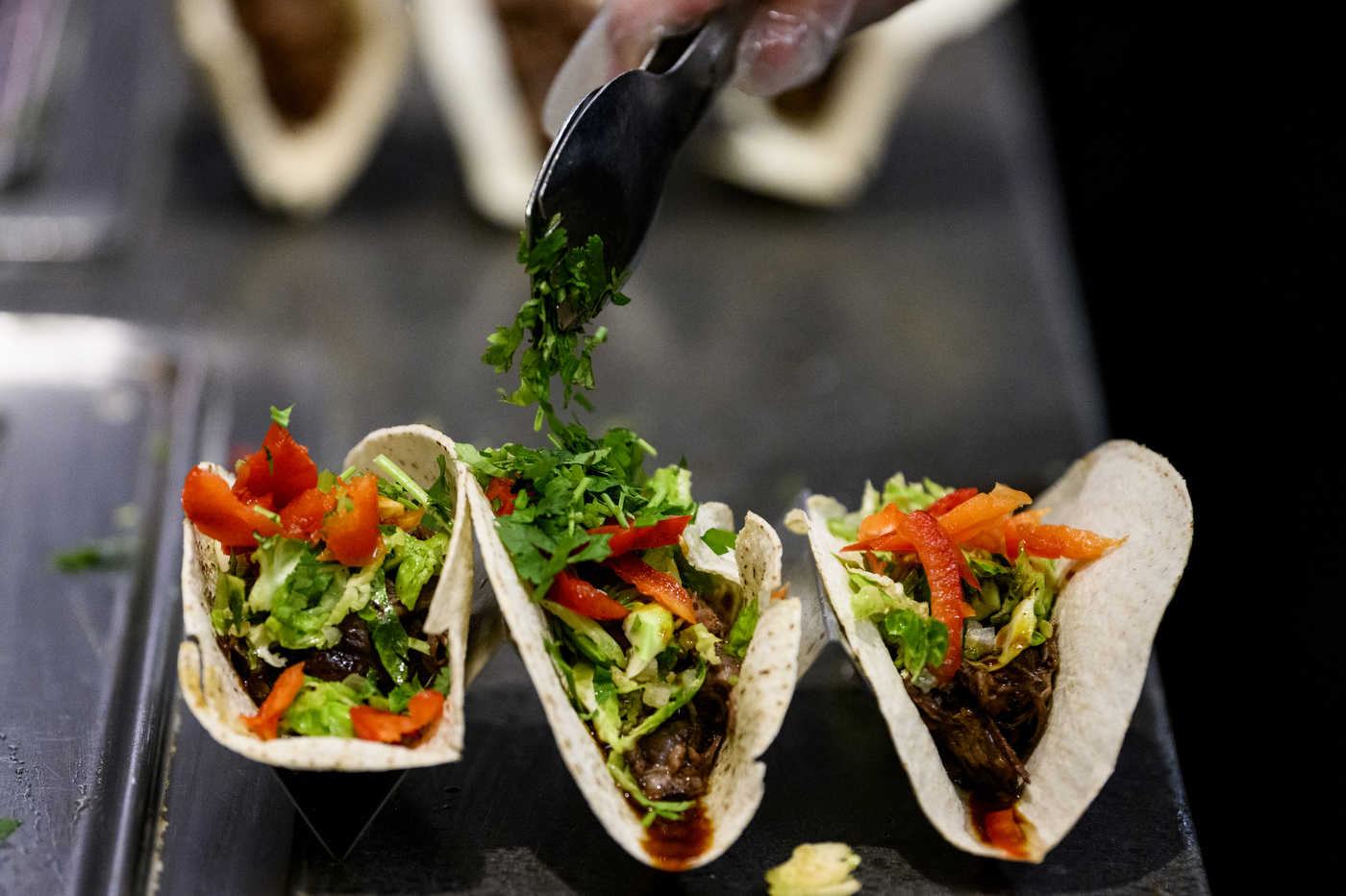 three tacos being garnished with chopped greens