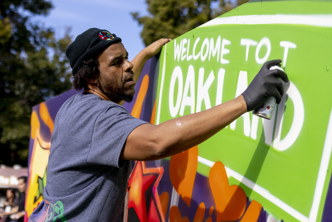 a person spray paints a sign that says 'welcome to Oakland'