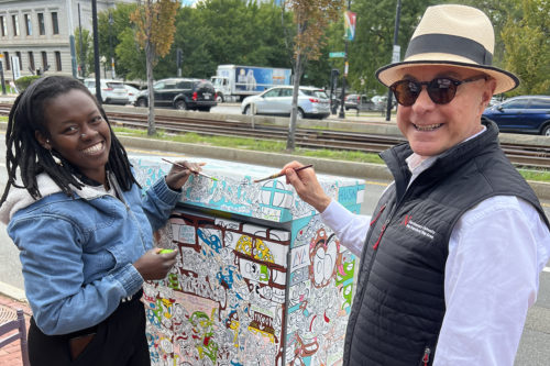 Northeastern University President Joseph E. Aoun helps Christy Charlot, a 2020 Northeastern graduate who majored in psychology, paint a mural on the box on the sidewalk near Cargill Hall at Northeastern’s School of Law. Charlot has been commissioned by the city of Boston to paint the box. Courtesy photo 