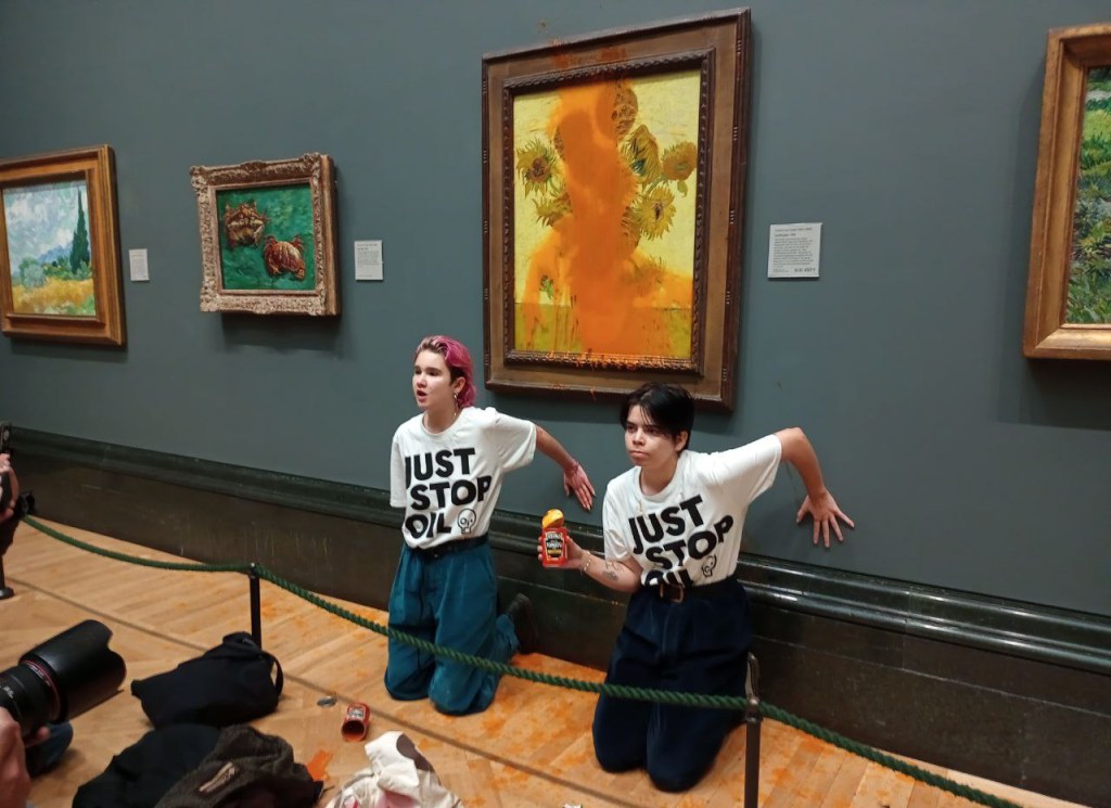 two protestors kneeling in a museum exhibit with their hands glued to the wall