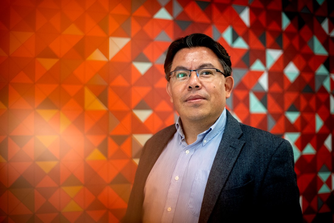 Portrait of Mauricio Santillana on a red geometric background.