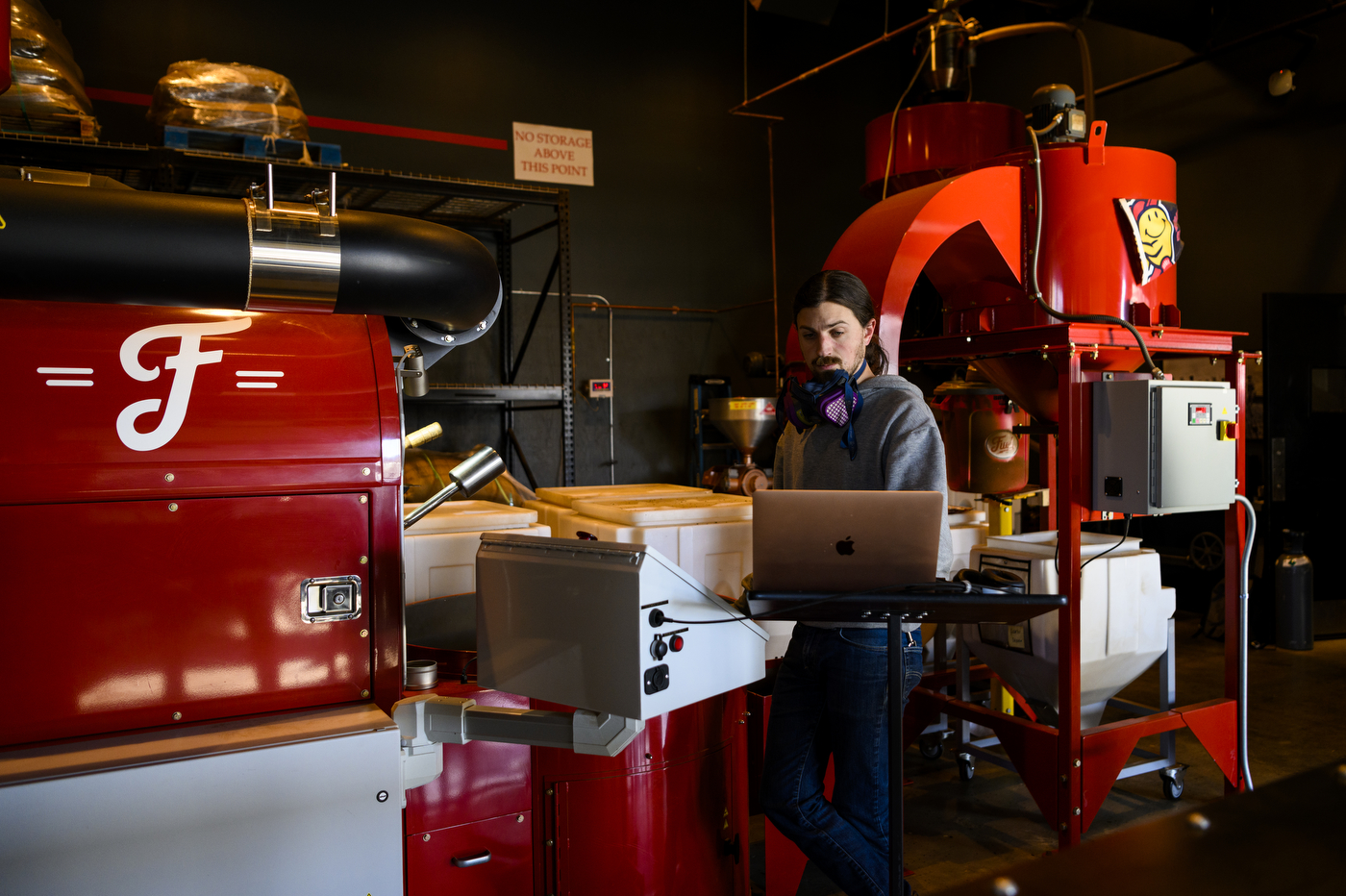 An employee glances at a laptop screen while operating a large red coffee-making machine within Fuel America.